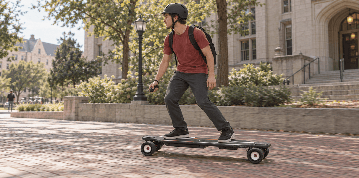 A helmeted rider with a backpack rides a Maxfind Cyber Max X along a textured brick path on campus.
