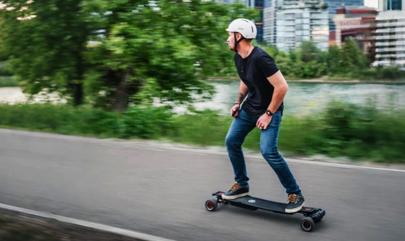 A man wearing a white safety helmet uses an electric skateboard on the road.